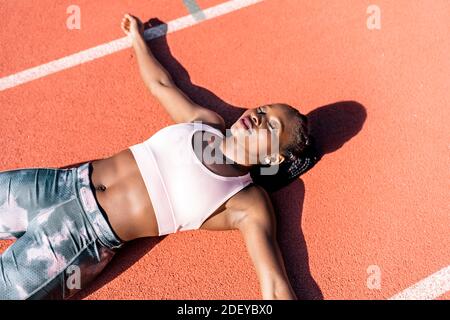 Foto d'inventario di un velocista afroamericano sdraiato su un pista atletica esaurita Foto Stock