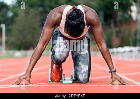 Foto d'inventario di un velocista afroamericano irriconoscibile in posizione di partenza per iniziare a correre su una pista atletica Foto Stock