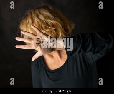 Una donna bionda copre il suo volto con una mano sulla quale ha scritto la parola Stop, per fermare la violenza contro le donne Foto Stock