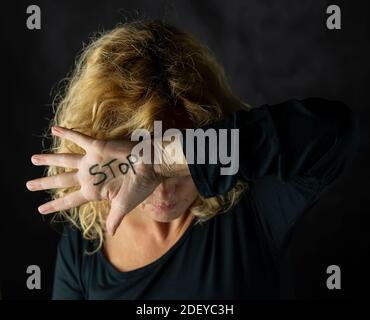 Una donna bionda copre il suo volto con una mano sulla quale ha scritto la parola Stop, per fermare la violenza contro le donne Foto Stock
