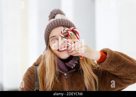 Ragazza in abiti invernali e un cappello tiene due caramelle caramello caramelle canne e facendo forma del cuore. Messa a fuoco superficiale e sfondo sfocato. Foto Stock