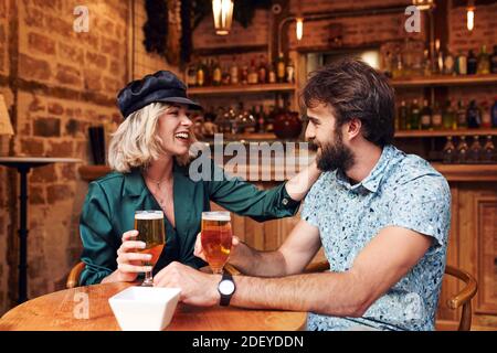 Foto di scorta di una coppia nei suoi 30 anni che beve un drink in un bar. Sorridono e ridono. Indossano un panno casual. Foto Stock