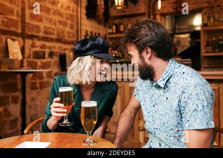 Foto di scorta di una coppia nei suoi 30 anni che beve un drink in un bar. Sorridono e ridono. Indossano un panno casual. Foto Stock