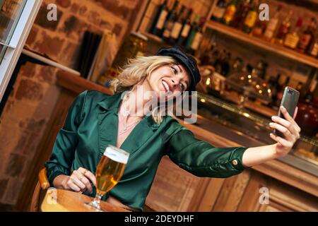 Foto di stock di una donna bionda nei suoi 30 anni prendendo un selfie. Indossa un panno casual e un cappello. Foto Stock