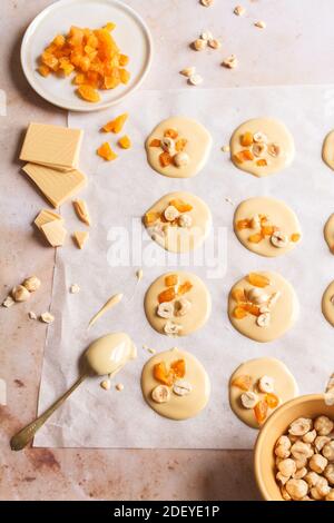 Dolci al cioccolato biondo fresco con nocciole e albicocche preparate su un pezzo di carta da forno. Foto Stock