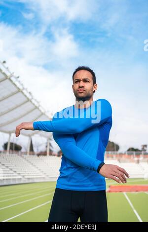 Foto di stock di atleta africano-americano maschio in piedi sulla pista che allunga le braccia, Foto Stock