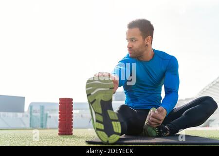 Foto d'inventario dell'atleta africano-americano seduto sul tracciato che allunga le gambe. Foto Stock