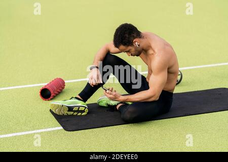 Scatta una foto di un atleta afro che fa una pausa mentre usa il telefono in pista sportiva. Foto Stock