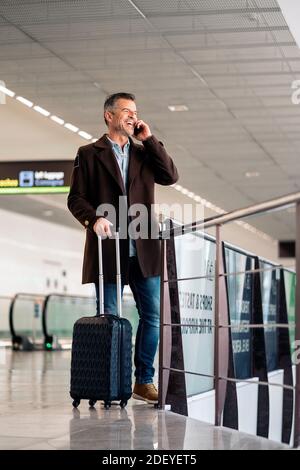 Stock foto di un uomo d'affari caucasico al telefono ridendo e andando a prendere un volo. Sta guardando un lato. Indossa abiti casual. Foto Stock