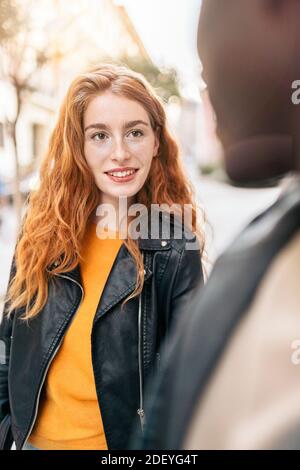 Foto d'inventario della giovane coppia multietnica che si guarda l'un l'altro mentre si cammina per la strada. Foto Stock