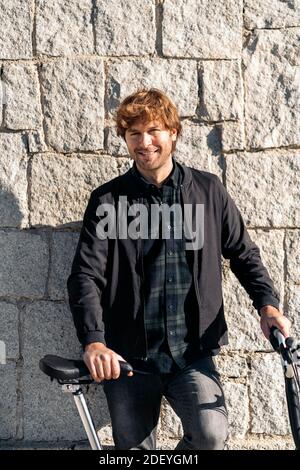 Scatta una foto del bell'uomo in piedi e guarda la fotocamera accanto alla sua bici staccabile. Foto Stock