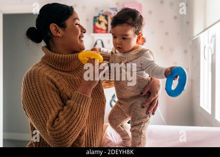 Stock foto di donna smiley che tiene il suo bambino piccolo e giocare con i giocattoli. Foto Stock