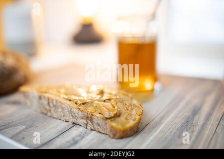 Fetta di pane con burro di arachidi e un vasetto di miele su tavolo di legno Foto Stock