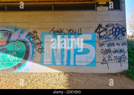 Un'opera d'arte dipinta in modo crudele raffigurante 'Thank You NHS' su un muro di cemento tra altri graffiti di Street art, Surrey England UK Foto Stock