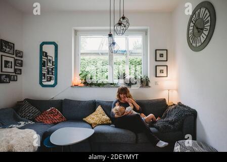 Allattamento materno e bambino sul divano nel soggiorno una casa accogliente Foto Stock