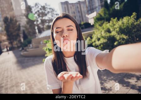 Ritratto fotografico di ragazza che invia bacio aria prendendo selfie tenendo con una mano in parcheggio Foto Stock