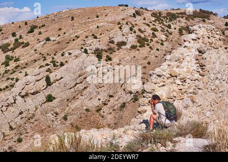 Il turista maschile asiatico anziano con uno zaino scatta foto sulla macchina fotografica sullo sfondo di un pendio di montagna in estate. Foto Stock