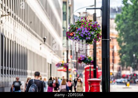 Londra, Regno Unito edifici e cestini di fiori appesi con persone in background sfocato sulla strada in estate con fiori colorati Foto Stock