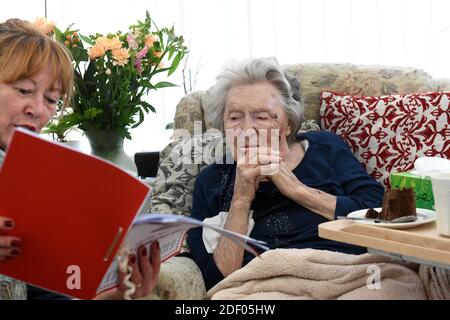 Donna che legge alla sua madre anziana che celebra il suo 104th compleanno in casa di cura Gran Bretagna, Regno Unito. Foto Stock