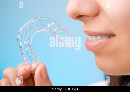 Primo piano donna che tiene una bretelle trasparenti rimovibili per un sorriso perfetto su sfondo blu. Allineatori ortodontici per raddrizzare e sbiancare Foto Stock