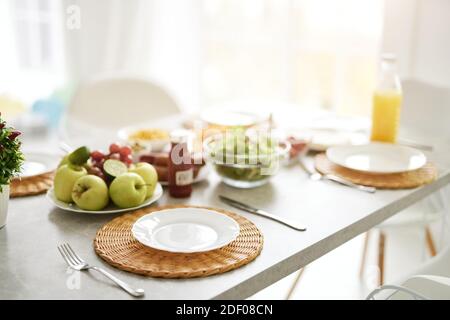 Primo piano di un piatto bianco vuoto e colazione in stile latino sul tavolo. Interni moderni e luminosi con cucina bianca e dettagli in legno e bianco. Mattina, idee per la colazione. Messa a fuoco selettiva Foto Stock