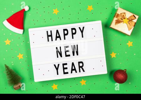 Felice anno nuovo testo in una scatola di luce, decorazioni e glitter su sfondo verde Foto Stock