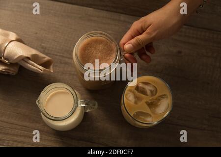 Caffè ghiacciato in vasetti e caraffa per il latte, piatto su fondo di legno. Foto Stock