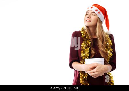 Giovane donna pensiva in un cappello di Babbo Natale, ha ricevuto un tanto atteso regalo di Natale su uno sfondo bianco. Natale Foto Stock