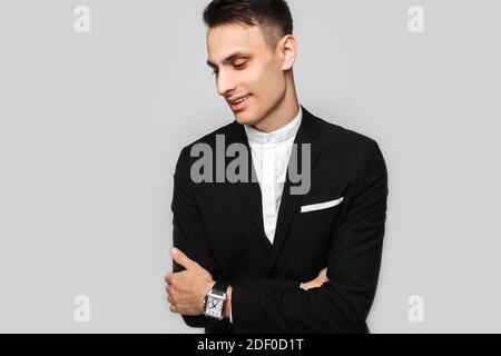 Ritratto di un giovane uomo d'affari, maschio, in una classica tuta nera, sorridente e guardante a lato, su sfondo grigio. Concetto di business, carriera. Foto Stock