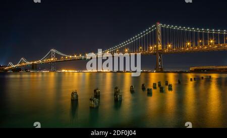 Immagine notturna dell'Oakland Bridge che lascia San Francisco e si dirige a nord-ovest verso Oakland con riflessi illuminati zavorre del molo sommerso Foto Stock