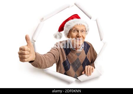 Uomo anziano con un cappello di babbo natale che si rompe attraverso la carta e facendo un segno di pollice in su Foto Stock