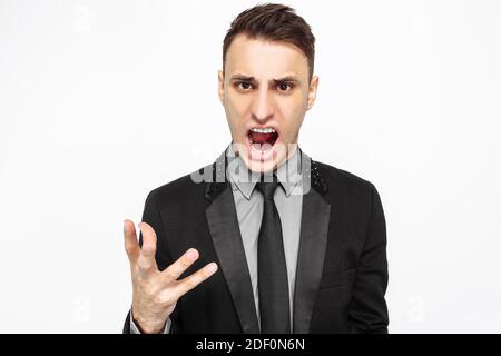 Un uomo depresso arrabbiato vestito con un vestito nero grida a qualcuno isolato su uno sfondo bianco. Un uomo in abito pieno esprime rabbia, grida lou Foto Stock