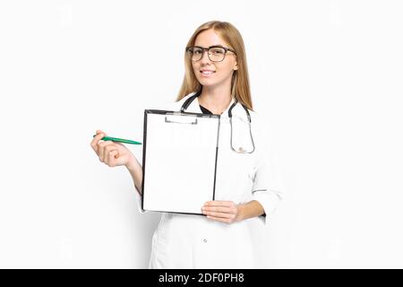 Giovane dottoressa in bicchieri e stetoscopio, che mostra una lima con un foglio di carta vuoto, su sfondo bianco. Concetto di medicina, spazio per la copia Foto Stock