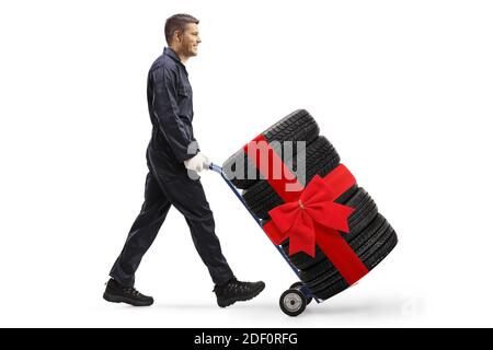 Scatto a tutta lunghezza di un meccanico che spinge un carrello a mano con pneumatici per auto legati da un nastro rosso isolato sfondo bianco Foto Stock