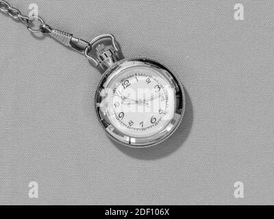 Piccolo orologio tascabile in acciaio con quadrante bianco, immagine in bianco e nero di oggetto metallico su sfondo uniforme Foto Stock