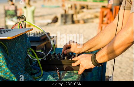 Primo piano su DJ che riproduce musica con attrezzature professionali tra cui console, computer portatile e amplificatore di potenza. Festa in spiaggia al tramonto Foto Stock