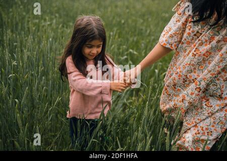 sorridente ragazza che tiene la mano delle mamme mentre cammina nel campo Foto Stock