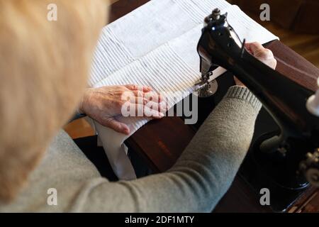 Donna anziana che usa una macchina da cucire d'epoca a casa Foto Stock