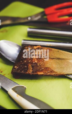 Una spatola di legno grassa e bruciata accanto all'altra cucina strumenti Foto Stock