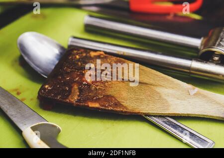 Una spatola di legno grassa e bruciata accanto all'altra cucina strumenti Foto Stock