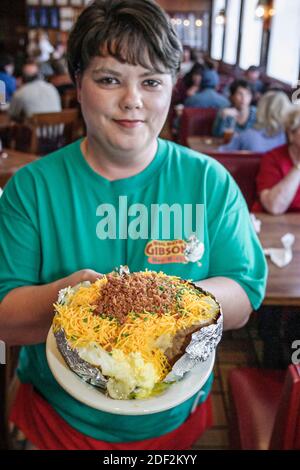 Alabama Decatur Big Bob Gibson BBQ ristorante, interno donna cameriera server donna donna cameriera che serve pollo di manzo di maiale, bar-b-q farcito patate al forno, Foto Stock