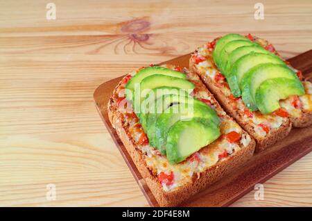 Un paio di toast fatti in casa alla griglia con pomodoro e avocado affettato su tavolo di legno Foto Stock