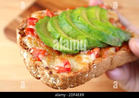 Preparare un appetitoso toast al formaggio grigliato con pomodoro e affettato avocado fresco in mano Foto Stock