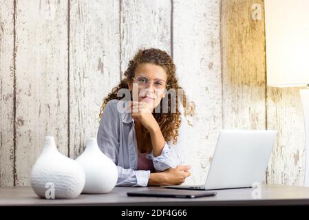 Bella donna che lavora da casa con un computer portatile che guarda dentro la fotocamera Foto Stock
