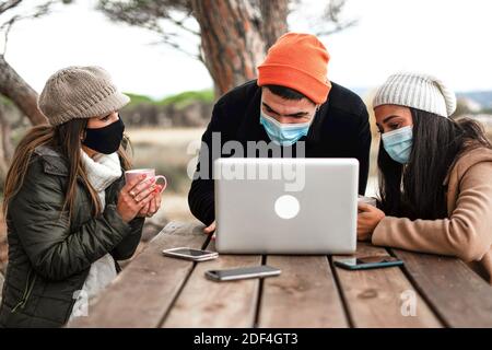 Hipster giovane uomo con notebook in alluminio su un tavolo di legno All'aperto con le sue due fidanzate che indossano la maschera di protezione sicura Coronavirus - Millennial pe Foto Stock