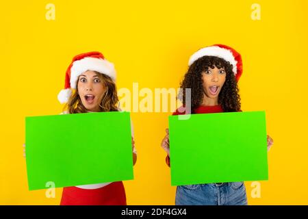 Banner divertente orizzontale di Natale con due donne di razza mista con bocca e occhi spalancati nell'espressione sorprendo che tiene verde Carrello per spazio di copia ad Foto Stock