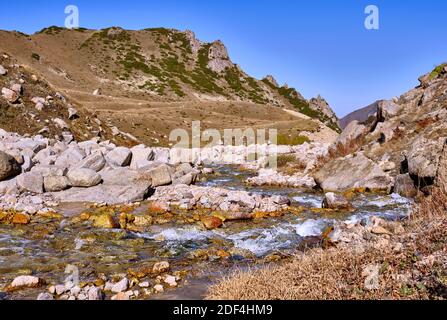 Valle alpina con fiume e pendii ricoperti di ginepro sul sfondo di cielo blu nella stagione autunnale Foto Stock