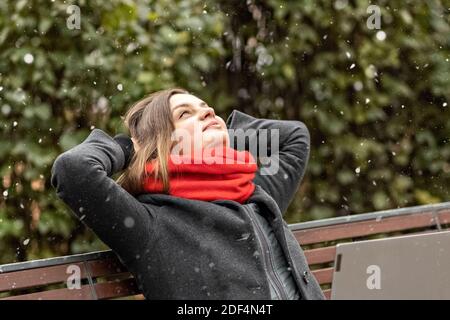 Una giovane donna, con le mani dietro la testa, sente la pace, si riposa dopo il lavoro, si siede su una panchina di legno nel parco un computer portatile sulle ginocchia. Si rompe durante w Foto Stock