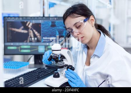 La scienziata femminile nel laboratorio moderno usa il microscopio per la medicina vacine. Tecnico medico che indossa un camice bianco in un laboratorio sterile che esegue l'analisi della soluzione. Foto Stock