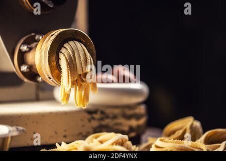 Pasta fresca di fettuccine lasciando la macchina per la preparazione della pasta. Foto Stock